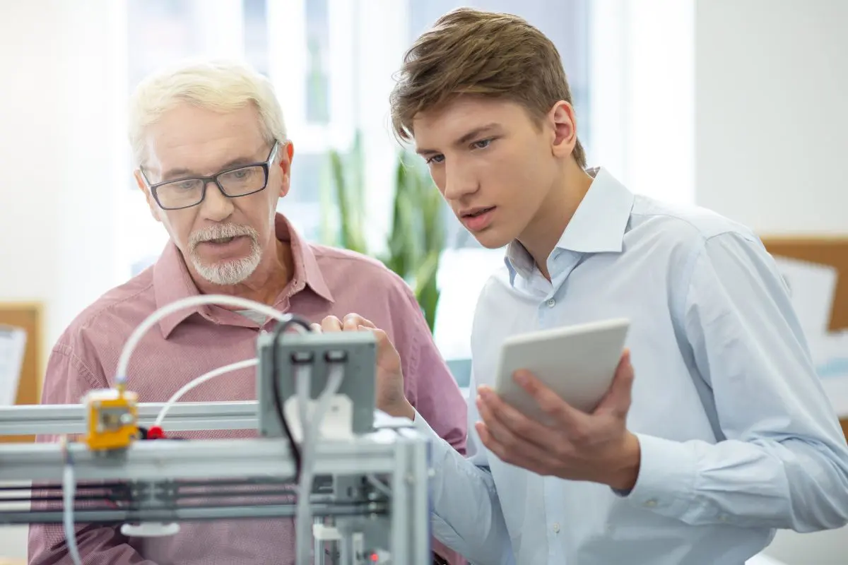 Two men examining 3D printer with tablet.